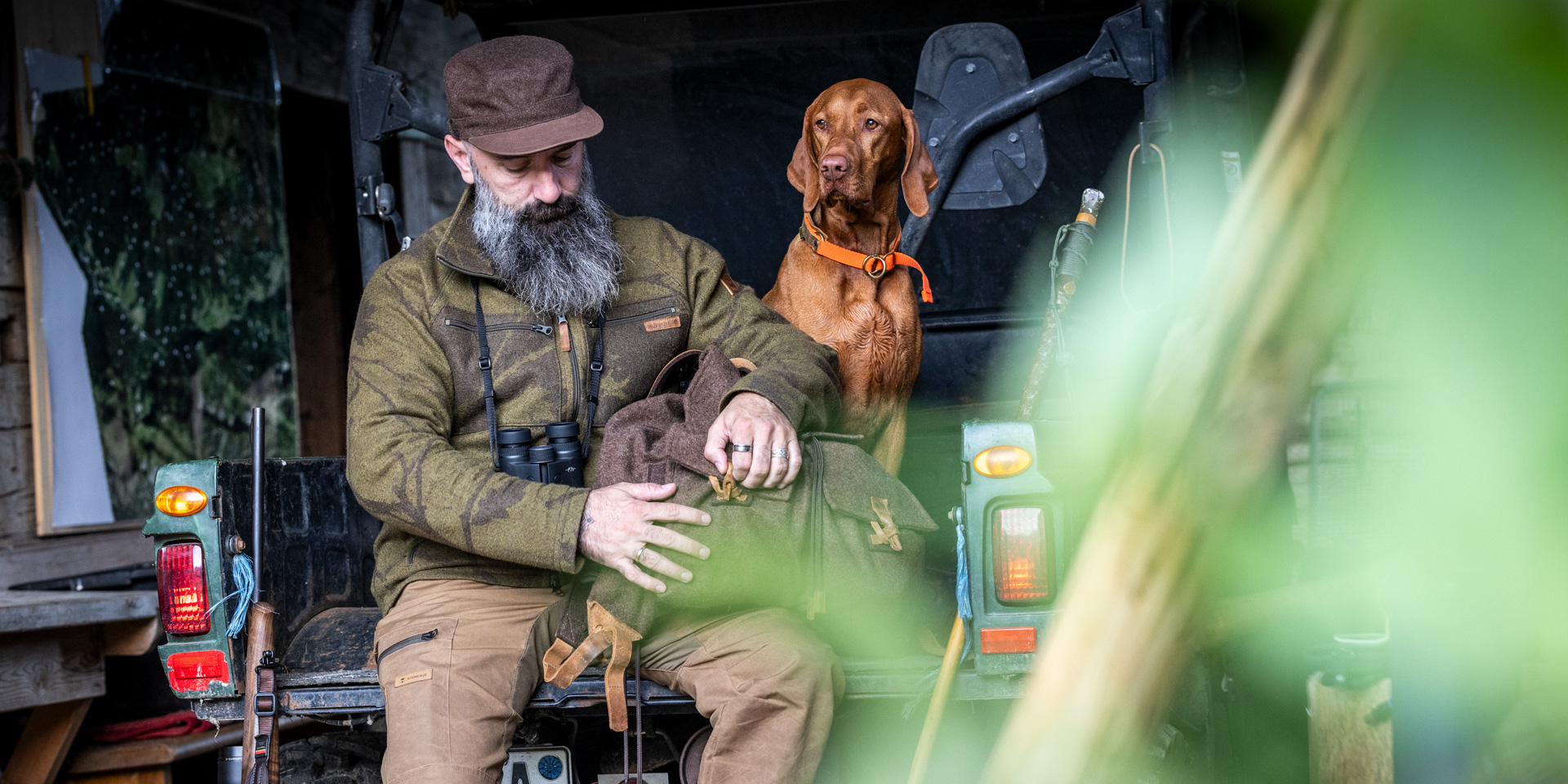 Jäger mit Rucksack und Hund auf Ladeklappe eines Jeeps