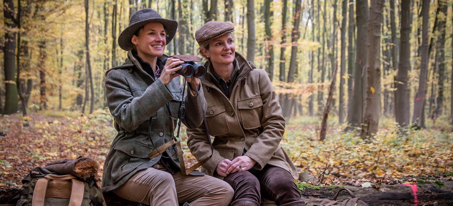 Zwei Jägerinnen sitzen auf Baumstamm Zwei Jägerinnen im Herbstwald